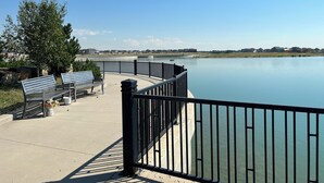 Eine Uferpromenade mit Bänken und Geländer, die auf einen ruhigen See blickt, mit Häusern im Hintergrund.