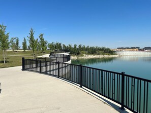 A waterfront park with a concrete walkway, metal railing, and a calm lake.