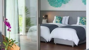 A modern bedroom with a large bed, a glass door leading to a balcony, and a view of greenery outside. - Malaiwana - Duplex (B2) by Elite Havens (A. Thalang)