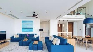 A modern living room with a blue sofa set, a coffee table, and a painting of a beach. - Malaiwana - Duplex (B2) by Elite Havens (A. Thalang)