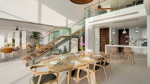 A spacious dining area with a wooden table set for six, a glass staircase, and a kitchen area visible in the background. - Malaiwana - Duplex (A3) by Elite Havens (A. Thalang)