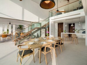 Ein geräumiger Essbereich mit einem Holztisch, gedeckt für sechs Personen, einer Glastreppe und einem sichtbaren Küchenbereich im Hintergrund.