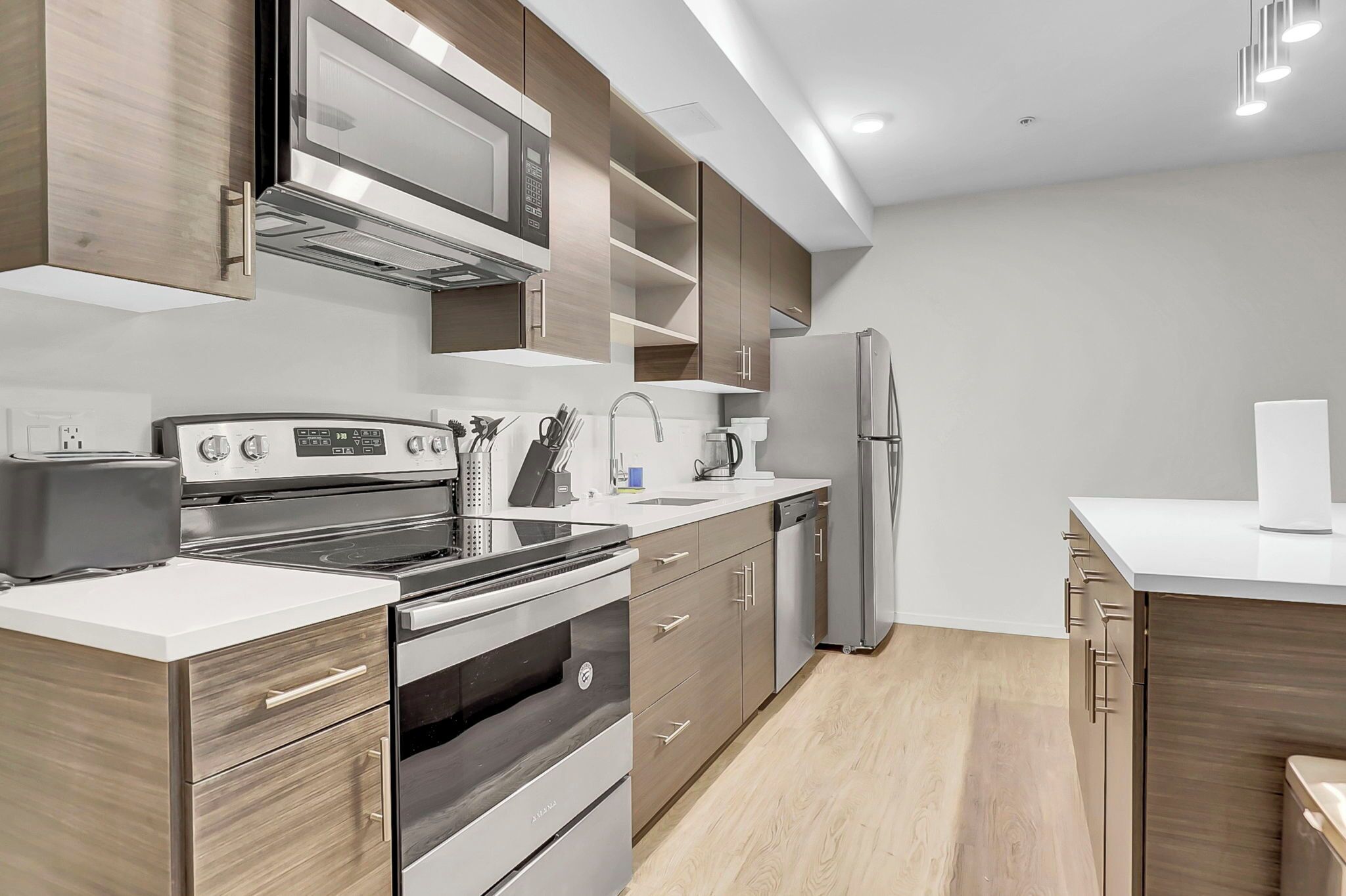 A modern kitchen with stainless steel appliances, wooden cabinets, and a white countertop.