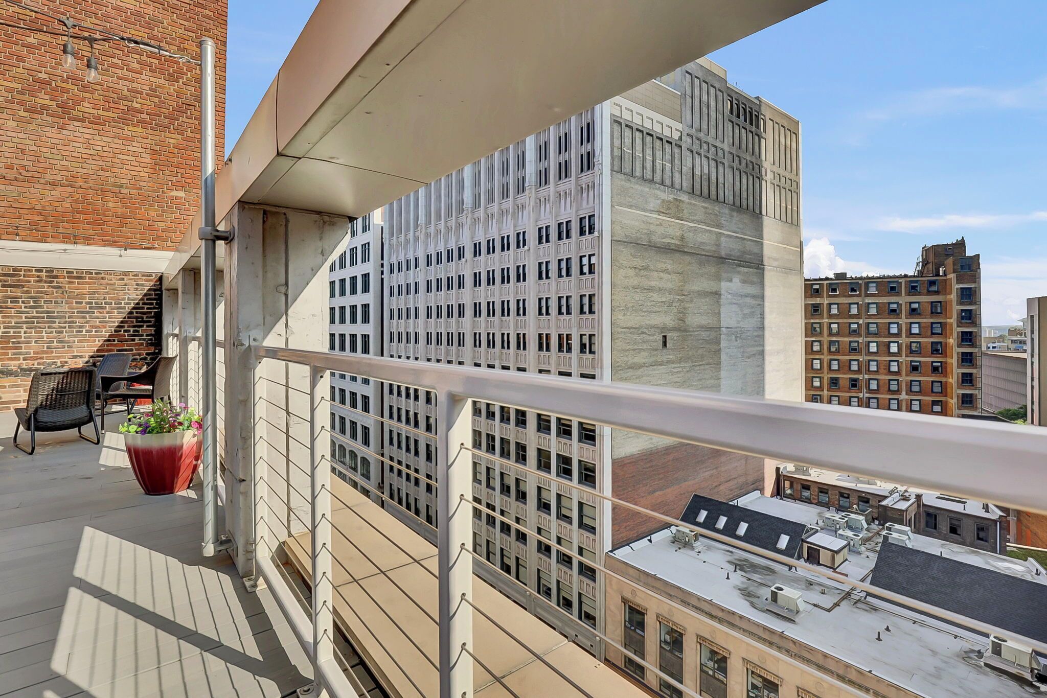 A balcony with a view of a modern building, a potted plant, and a table with chairs.