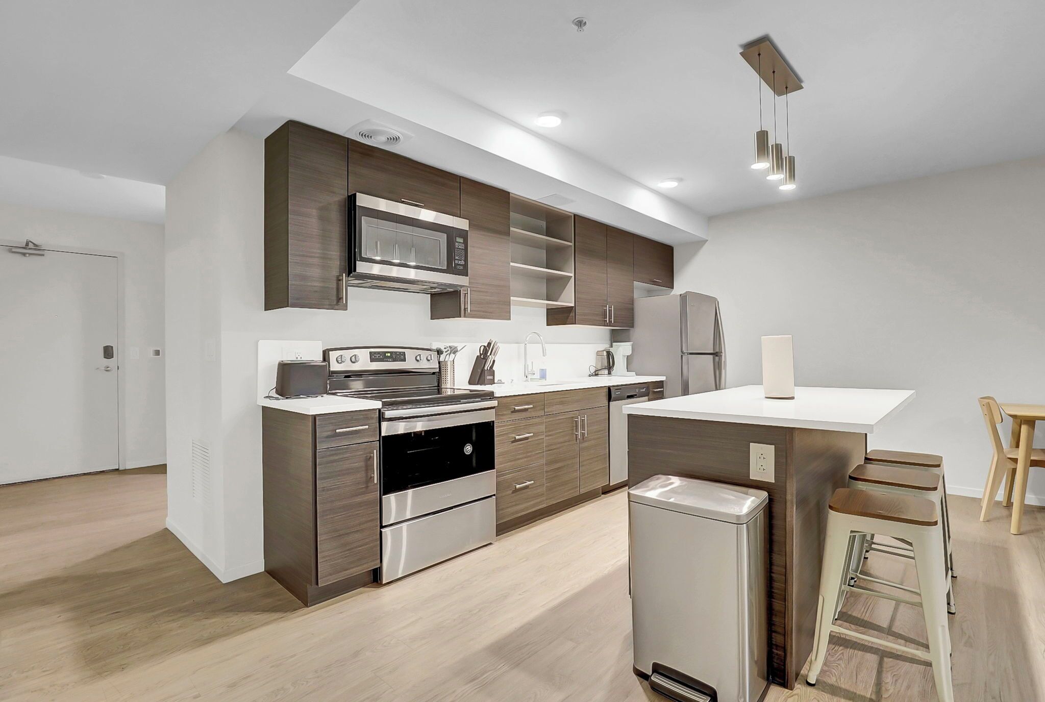 A modern kitchen with stainless steel appliances, wooden cabinetry, and a central island with stools.