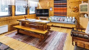 Een gezellig interieur van een chalet met een houten eettafel, een bankje, een bank en een televisie.