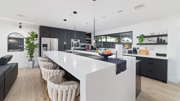 Una cocina moderna con una isla central, taburetes de bar e iluminación colgante.