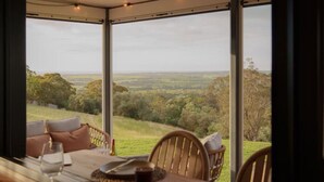 A dining area with a table set for two, overlooking a scenic landscape through large windows.