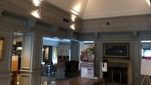 Un hall de hotel con mostrador de recepción, chimenea y un cuadro en la pared.