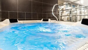 Un jacuzzi con agua cristalina, rodeado de tumbonas blancas y una barandilla metálica.