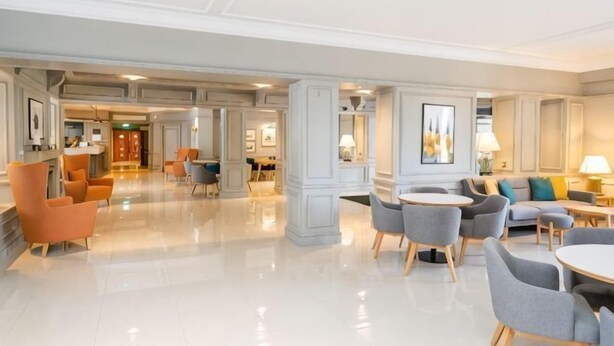 Un amplio vestíbulo de hotel con piso pulido, zonas de estar y un mostrador de recepción.