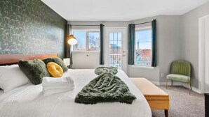 Habitación de hotel con una cama grande, un banco, una silla y vistas al exterior.