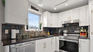 Una cocina moderna con armarios blancos, electrodomésticos de acero inoxidable y un ventanal que proporciona luz natural.