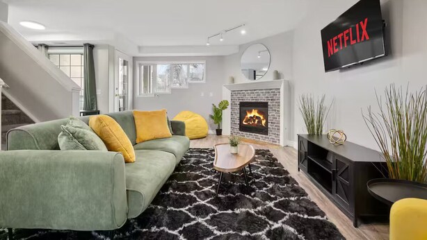 Un salón moderno con un sofá verde, una alfombra blanco y negro, una chimenea y un televisor montado en la pared mostrando 'NETFLIX'.
