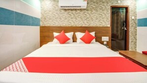 Quarto de hotel com cama, cabeceira de madeira, colcha vermelha e branca e ar condicionado fixado na parede.