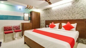 Quarto de hotel com uma cama grande, cabeceira de madeira e parede de pedra. Há duas cadeiras vermelhas e um guarda-roupa de madeira.