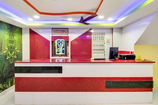 A reception desk with a modern design, including a red and white color scheme, a ceiling fan, and a decorative wall with a floral pattern.