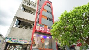 Um edifício de vários andares com uma fachada marcante em vermelho e cinza, apresentando uma placa com 'Hotel Sri G' e 'Sivaji Hair Styles' abaixo.