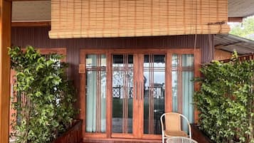 Une façade en bois avec une porte-fenêtre coulissante, une chaise en osier et des plantes en pot.