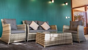 A seating area with wicker furniture and cushions, a glass coffee table, and teal walls with wall-mounted lights. - Ban Slow Life Homestay Koh Libong (Ko Libong)