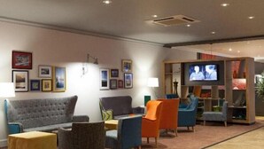 Ein stilvoller Lounge-Bereich mit grauem Sofa, bunten Sesseln, einem Flachbildfernseher und einem Bücherregal.