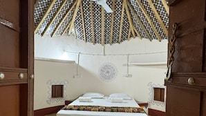 A room with a high, woven ceiling, a bed with a patterned bedspread, and a small window. - Rann Sanji Stay (Bhuj)