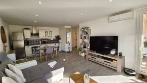 Ein modernes Wohnzimmer mit einem grauen Ecksofa, einem Holztisch und einem Flachbildfernseher auf einem Holzständer.