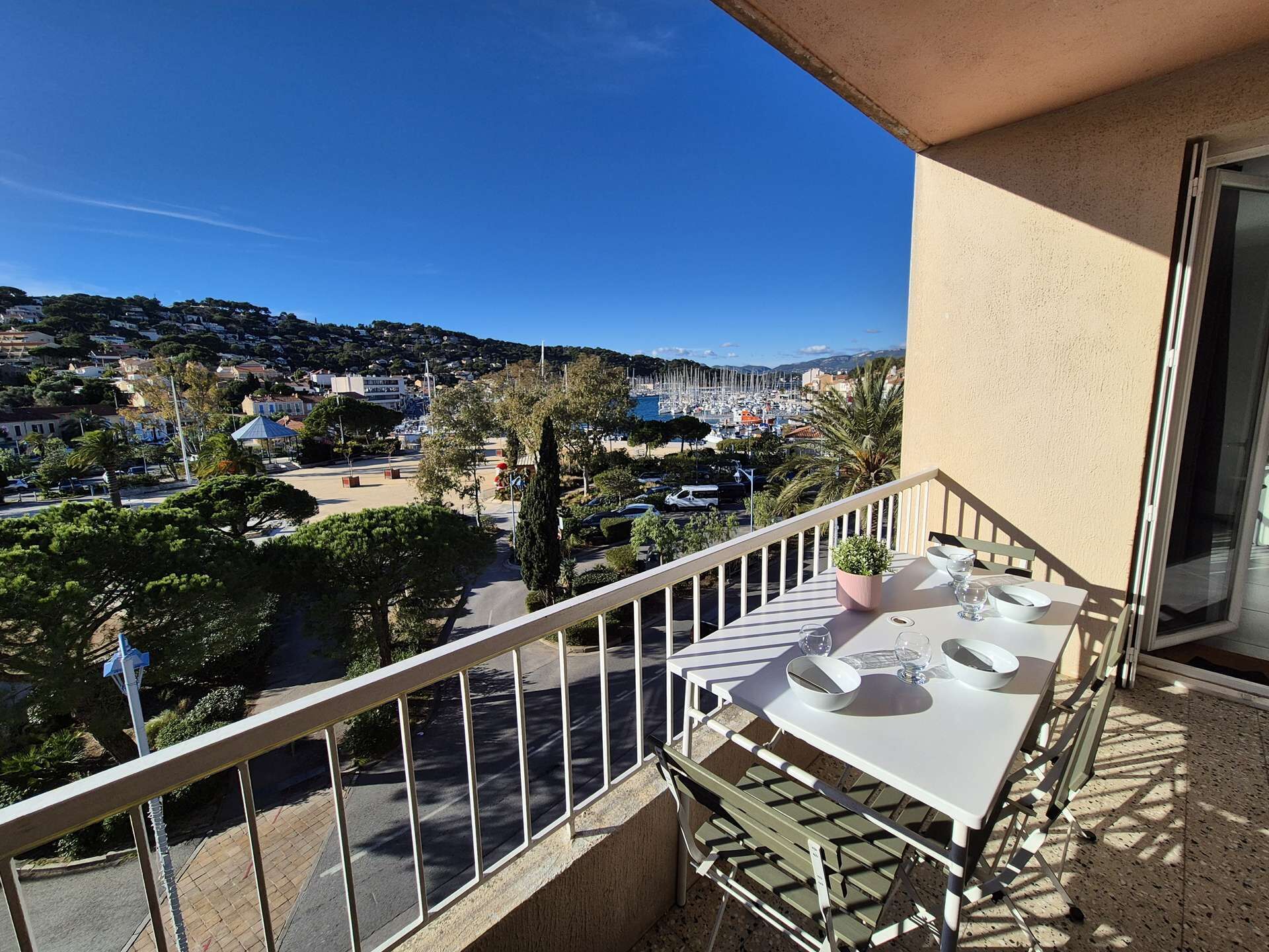 A balcony with a table and chairs, overlooking a marina and a coastal town.