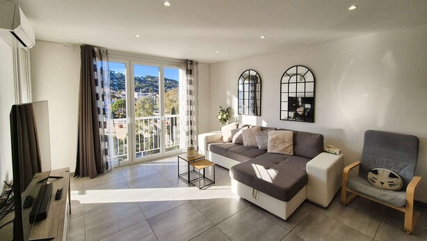 Ein modernes Wohnzimmer mit einer Couch, einem Sessel, einem Fernseher und einem Balkon mit Blick auf die Stadt.
