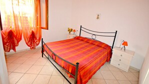 A bedroom with a bed, a nightstand, a dresser, and a window with curtains. - Appartamenti Granseola - Granseola -  Bilocale (Campo nell'Elba)