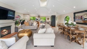 A spacious living room with a fireplace, a dining area with wooden chairs, and a large TV mounted on the wall. - The Pier Taupo (Taupo)