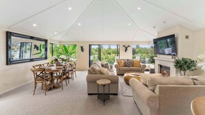A spacious living room with a high ceiling, a fireplace, a television, and a dining area with wooden furniture. - The Pier Taupo (Taupo)