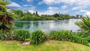 A serene lakeside view with lush greenery and a clear sky. - The Pier Taupo (Taupo)