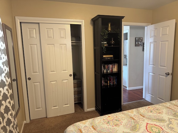 A bedroom with a bed, a wardrobe, a bookshelf, and a door leading to another room.