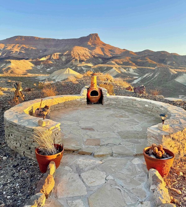 A stone patio with a central fire pit, surrounded by stone walls and potted plants.