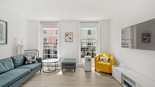 A modern living room with a sofa, ottoman, yellow armchair, and a flat-screen TV mounted on the wall. - Flat 1 Beauchamp Place (London)