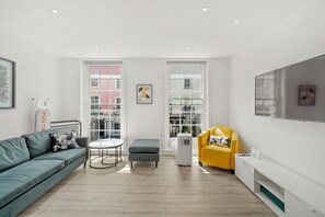 A modern living room with a sofa, ottoman, yellow armchair, and a flat-screen TV mounted on the wall. - Flat 1 Beauchamp Place (London)