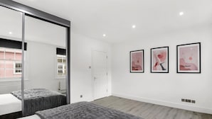 A modern bedroom with a large bed, a sliding glass door, and three framed artworks on the wall. - Flat 1 Beauchamp Place (London)