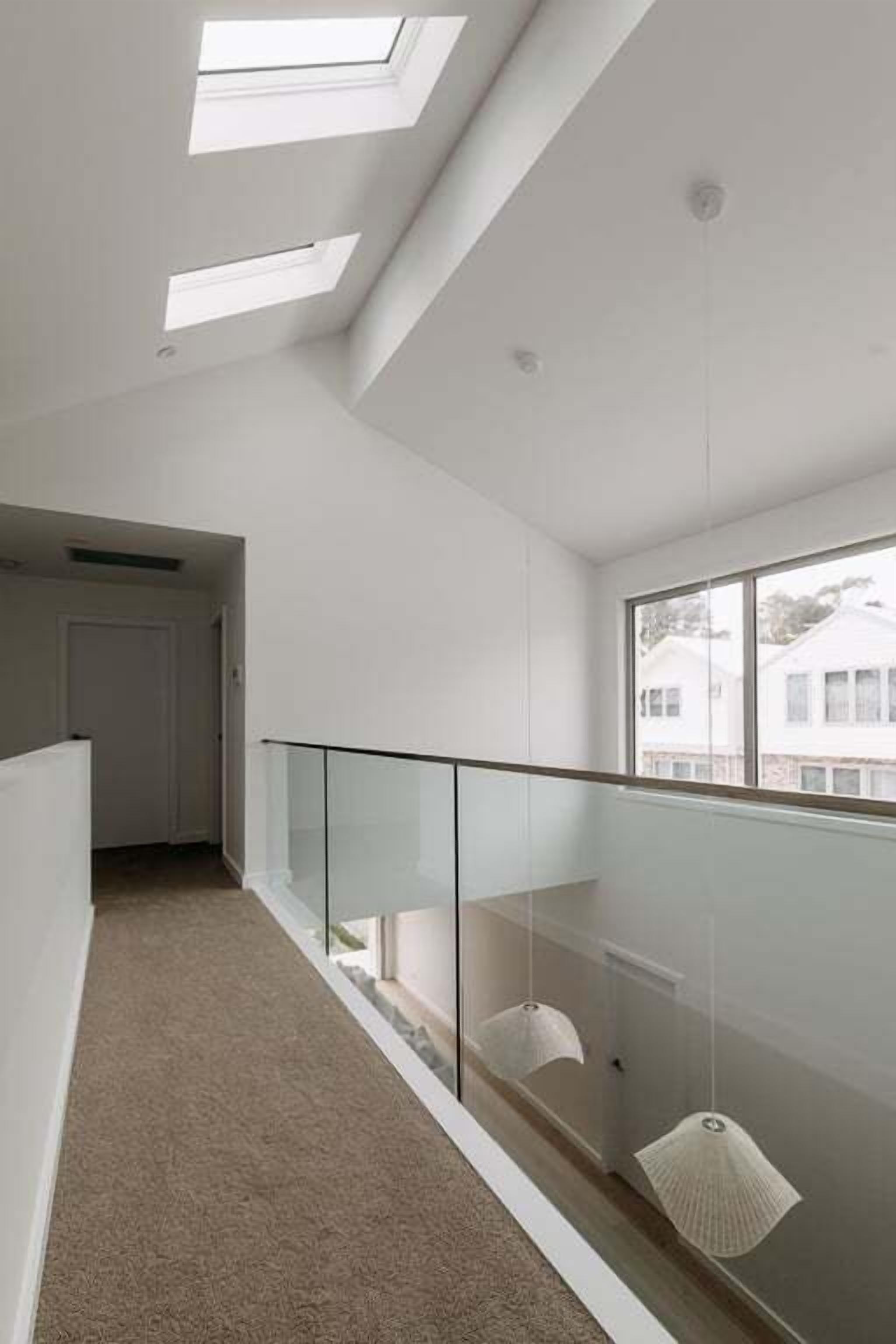 A modern interior with skylights, a glass railing, and a carpeted floor.