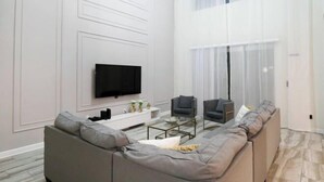 A modern living room with a large grey sofa, a flat-screen TV mounted on the wall, and a glass coffee table. - Themed 5Bd Home, Movie and Game Room (4726) (Kissimmee)