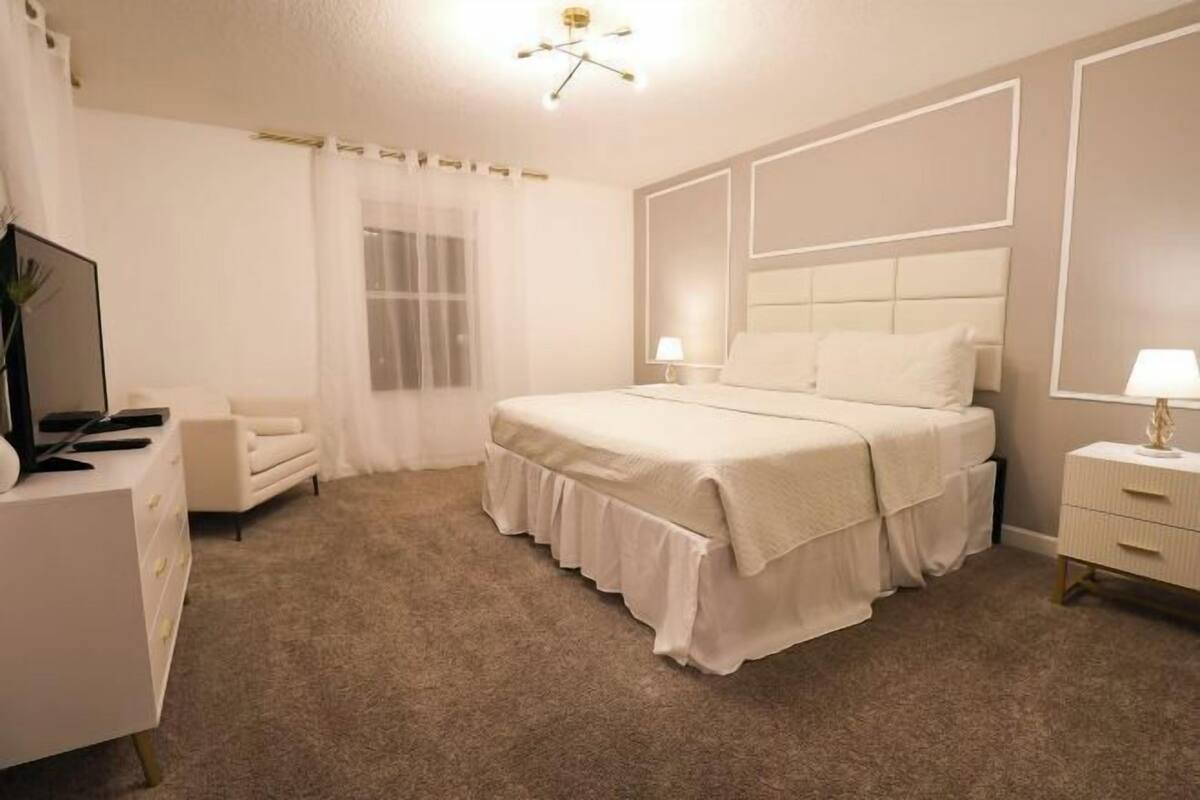 A bedroom with a bed, a dresser, a TV, and a window with curtains.