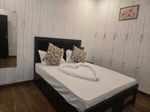 Un lit bien fait, avec un matelas blanc et deux coussins à motifs floraux, une tête de lit en bois et un plancher en bois.