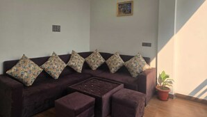 Ein Wohnzimmer mit einem dunkelbraunen Sofa, passendem Hocker und einem kleinen Tisch. Eine Topfpflanze befindet sich auf der rechten Seite.