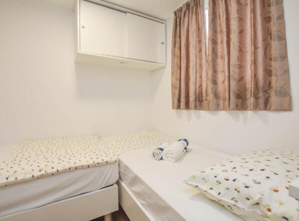 A small, single-room with two beds, a wardrobe, and a window with floral curtains. - Camping Mobile Homes Bella Vita Biograd na Moru (Biograd na Moru)