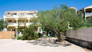 Un edificio a più piani con balconi, terreno sabbioso e un albero sullo sfondo.