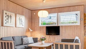 Een gezellige kamer met houten details, een bank, twee fauteuils, een ronde tafel, een televisie en lijstwerken.