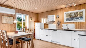 Een moderne keuken met houten lambrisering, witte kasten en een eethoek met houten stoelen en een tafel.