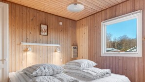 Een slaapkamer met houten paneelwanden, een bed met witte beddengoed, een raam met uitzicht op bomen en een plafondlamp.