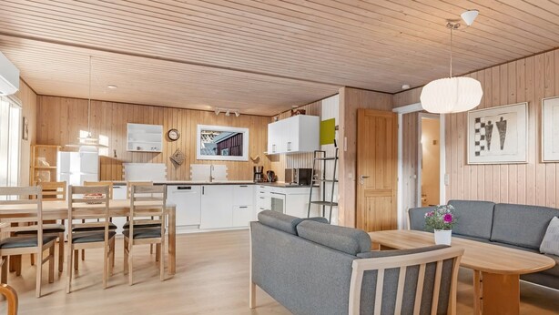Een moderne keuken met houten kasten, een eethoek met een houten tafel en stoelen, en een zithoek met een bank en salontafel.