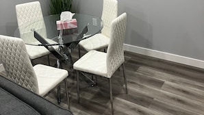 A modern meeting room with a glass table, white cushioned chairs, and a potted plant.